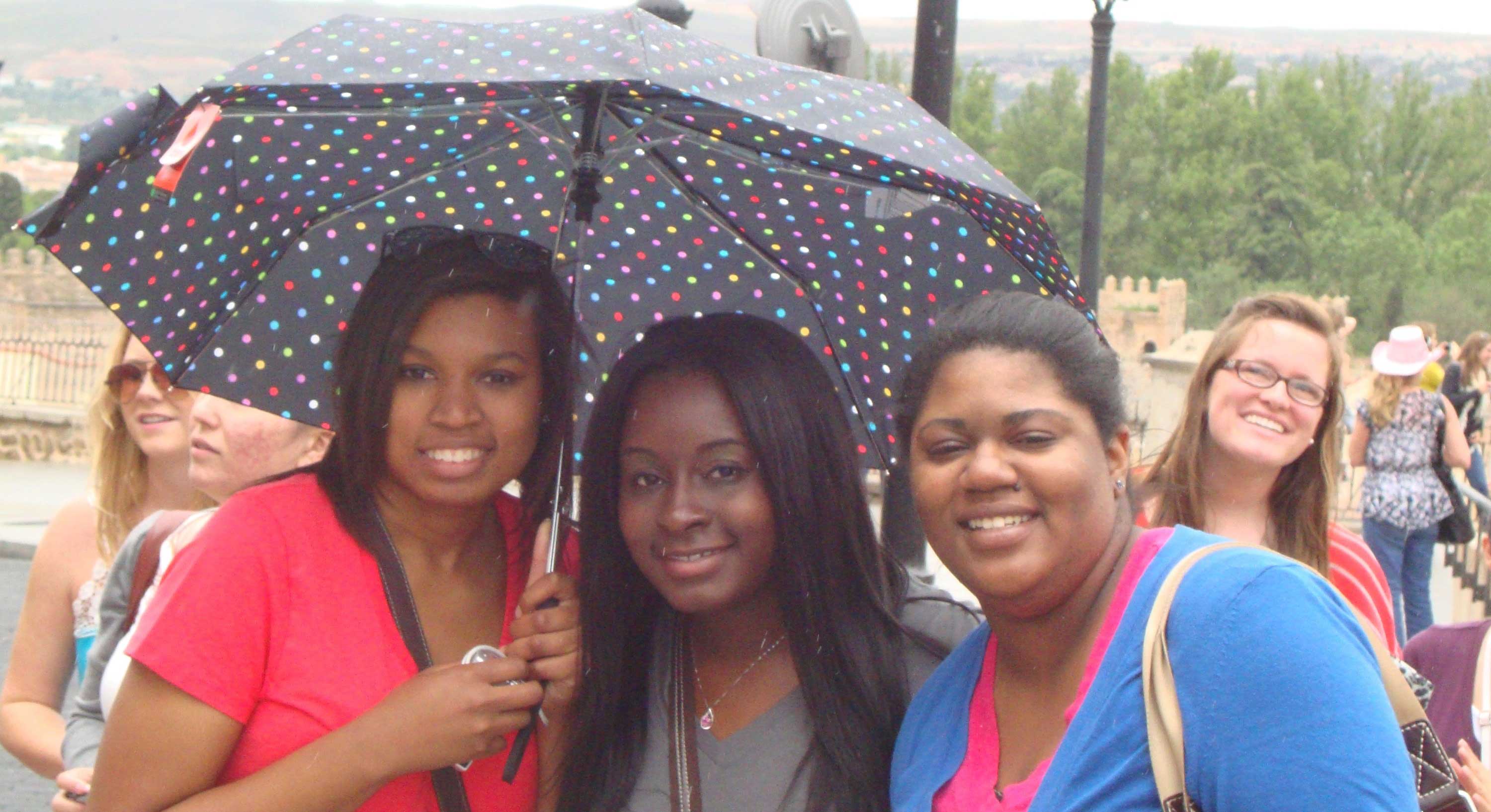 Three students in Spain with umbrella.